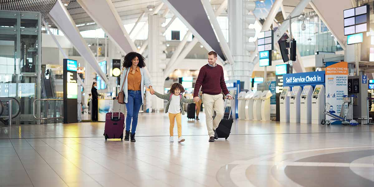 A joyful family with a child walks hand in hand through a bright airport terminal, pulling suitcases. The scene conveys excitement and warmth.